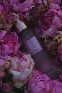a close up of a bottle of perfume surrounded by pink flowers