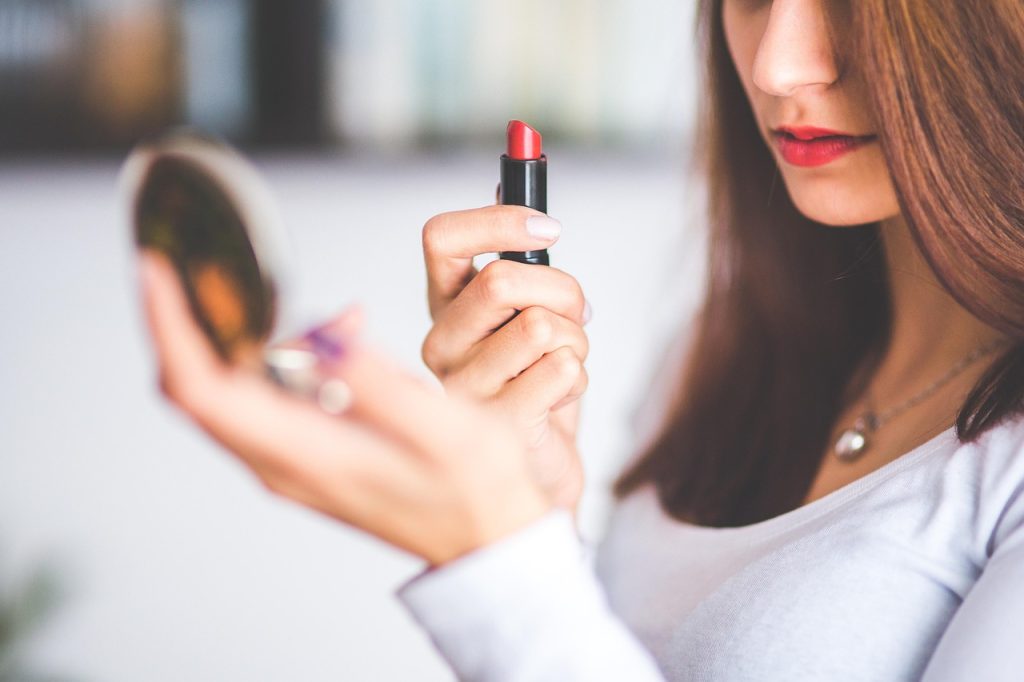 Vrouw die make-up aanbrengt voor een spiegel met verschillende schminkproducten op tafel
